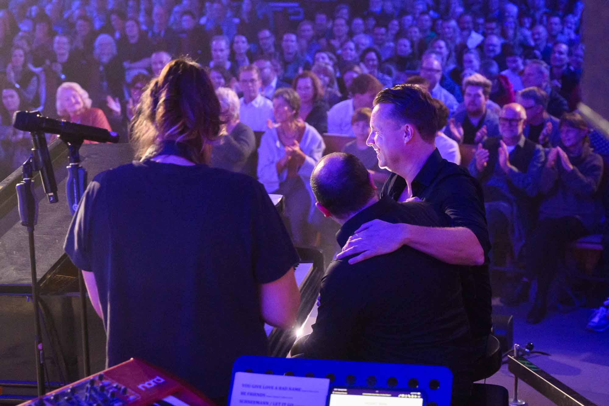 Umarmung auf der Bühne vor applaudierendem Publikum